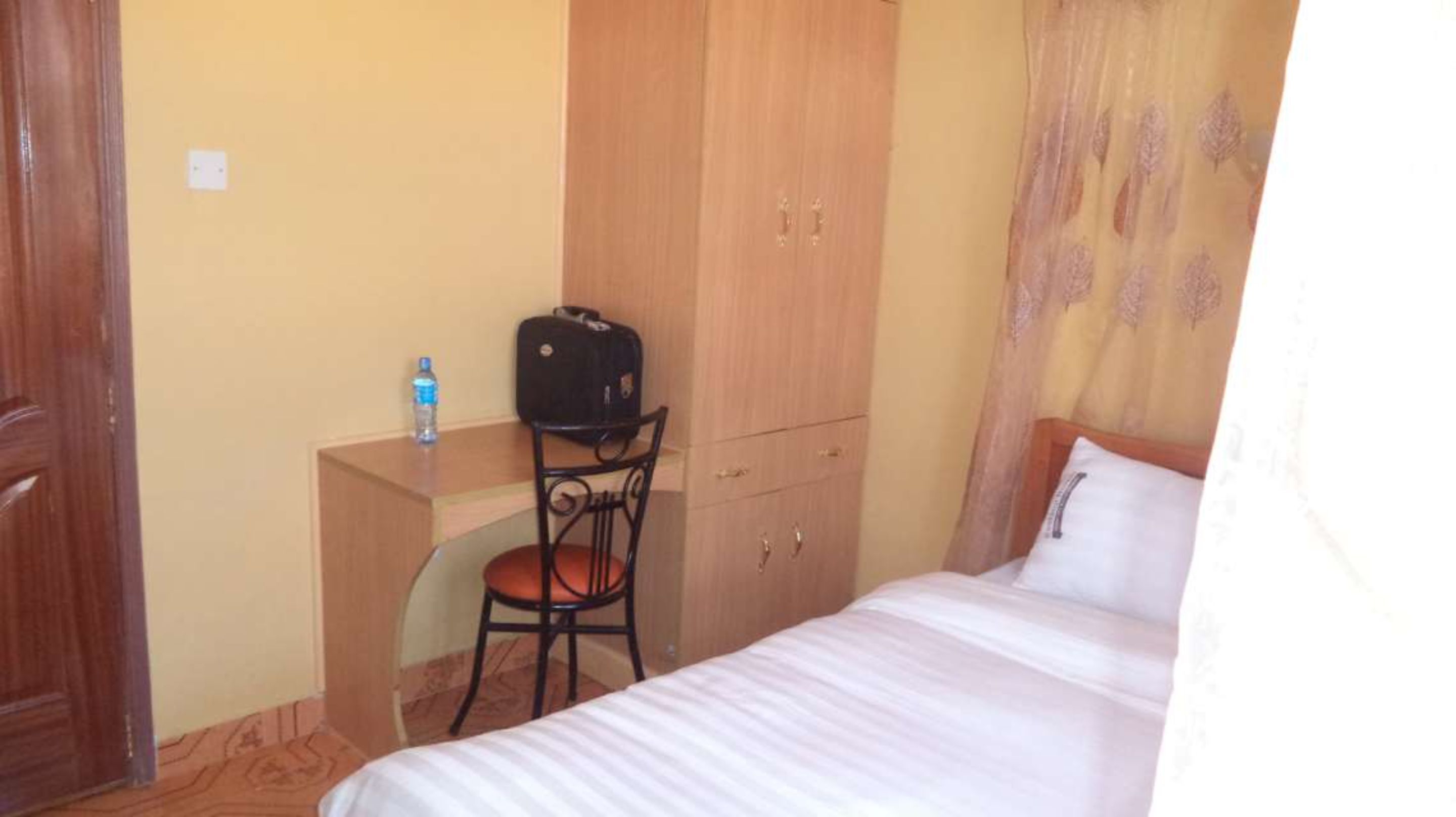 A bedroom with a bed, a desk with a chair, a wardrobe, and a water bottle on the desk.