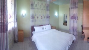 A bedroom with a bed, curtains, a nightstand, a wall-mounted light, and a mirror.