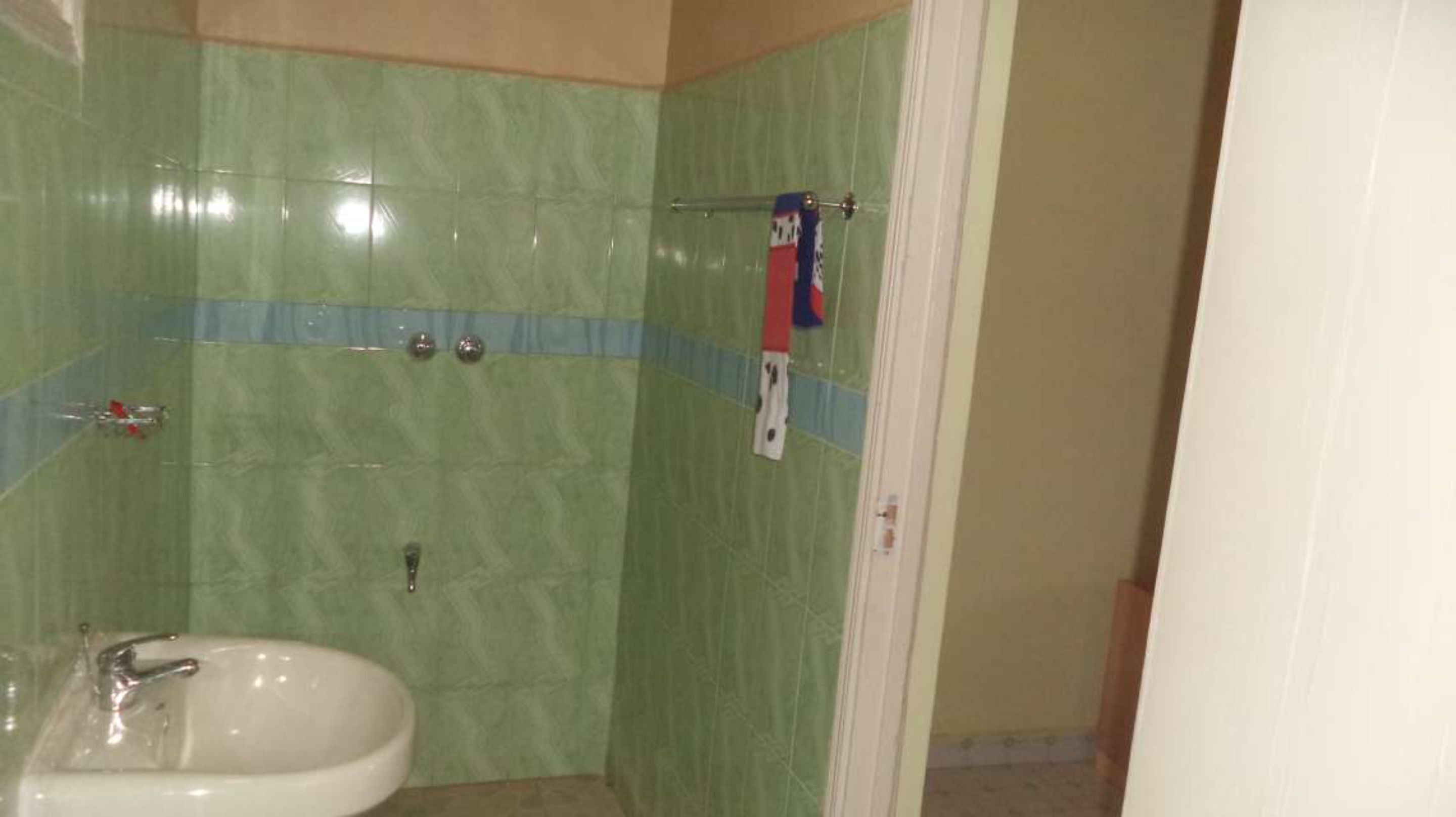A bathroom with green tiles, a white sink, and a shower area.