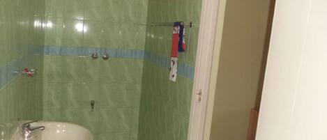 Un baño con azulejos verdes, un lavamanos blanco y zona de ducha.