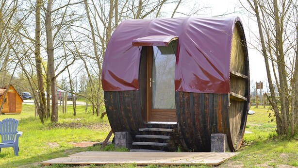 Una cabaña rústica con una estructura en forma de barril, una puerta de madera y una lona morada cubriendo el techo.