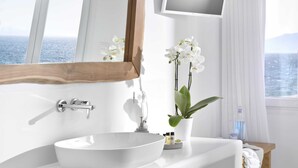 A bathroom with a white sink, a wooden-framed mirror, and a view of the sea through a window. - Marietta's Mykonos (Mykonos)