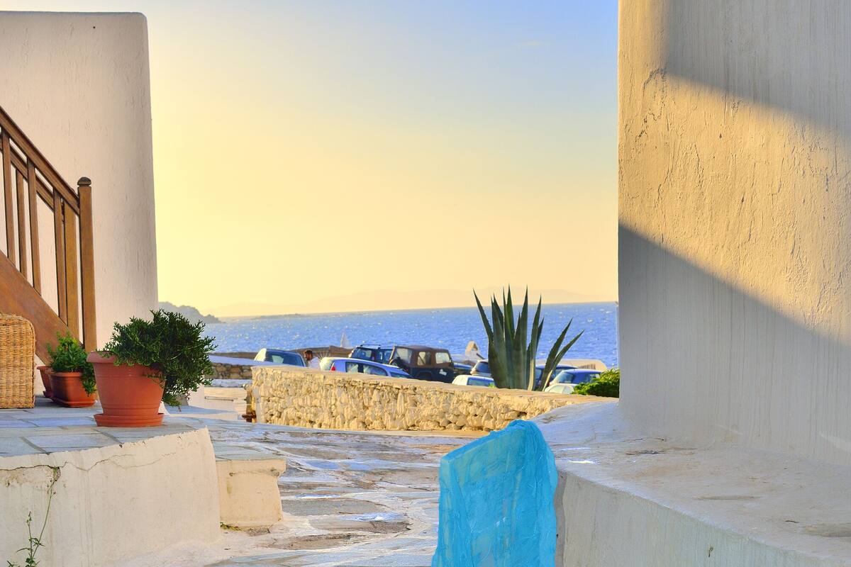 A stone-paved outdoor area with a white chair and a blue cloth, overlooking a beach with cars and a stone wall.