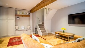 A spacious living area with a wooden ceiling, a staircase, a sofa, a wooden coffee table, and a TV mounted on the wall. - School Cottage (Holmfirth)