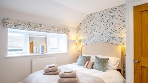 A bedroom with a large bed, a window with a view, a radiator, and a wooden door. - School Cottage (Holmfirth)