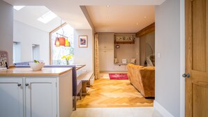 A modern kitchen with a dining area, wooden flooring, and a view of the city. - School Cottage (Holmfirth)