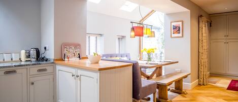 A modern kitchen with a wooden island, white cabinets, and a dining area with a bench and table.