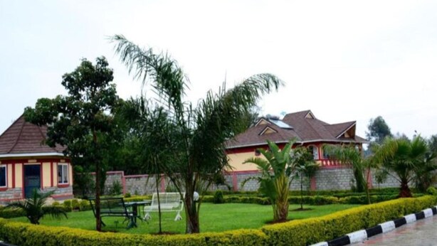 A building with a red and yellow facade, surrounded by well-maintained greenery and a paved walkway. - Eldoret Luxurious Furnished Homes (Eldoret)