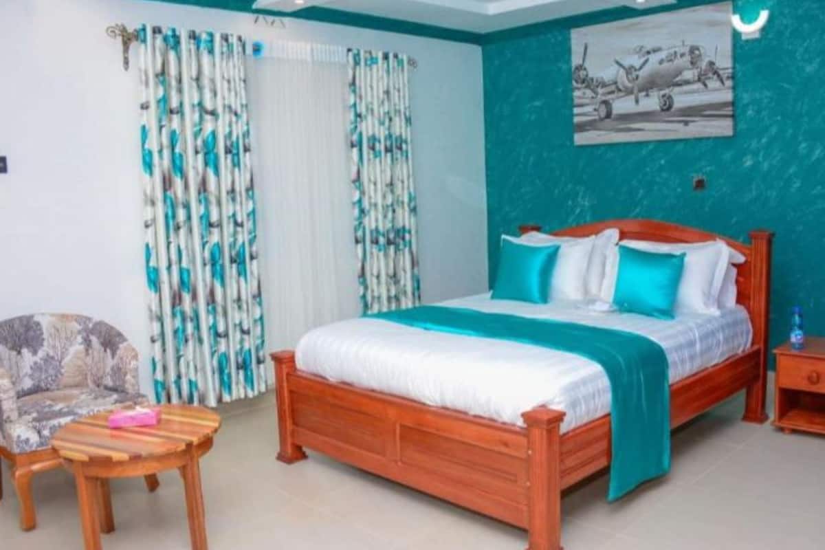 A bedroom with a wooden bed, a chair, a nightstand, and a painting on the wall.