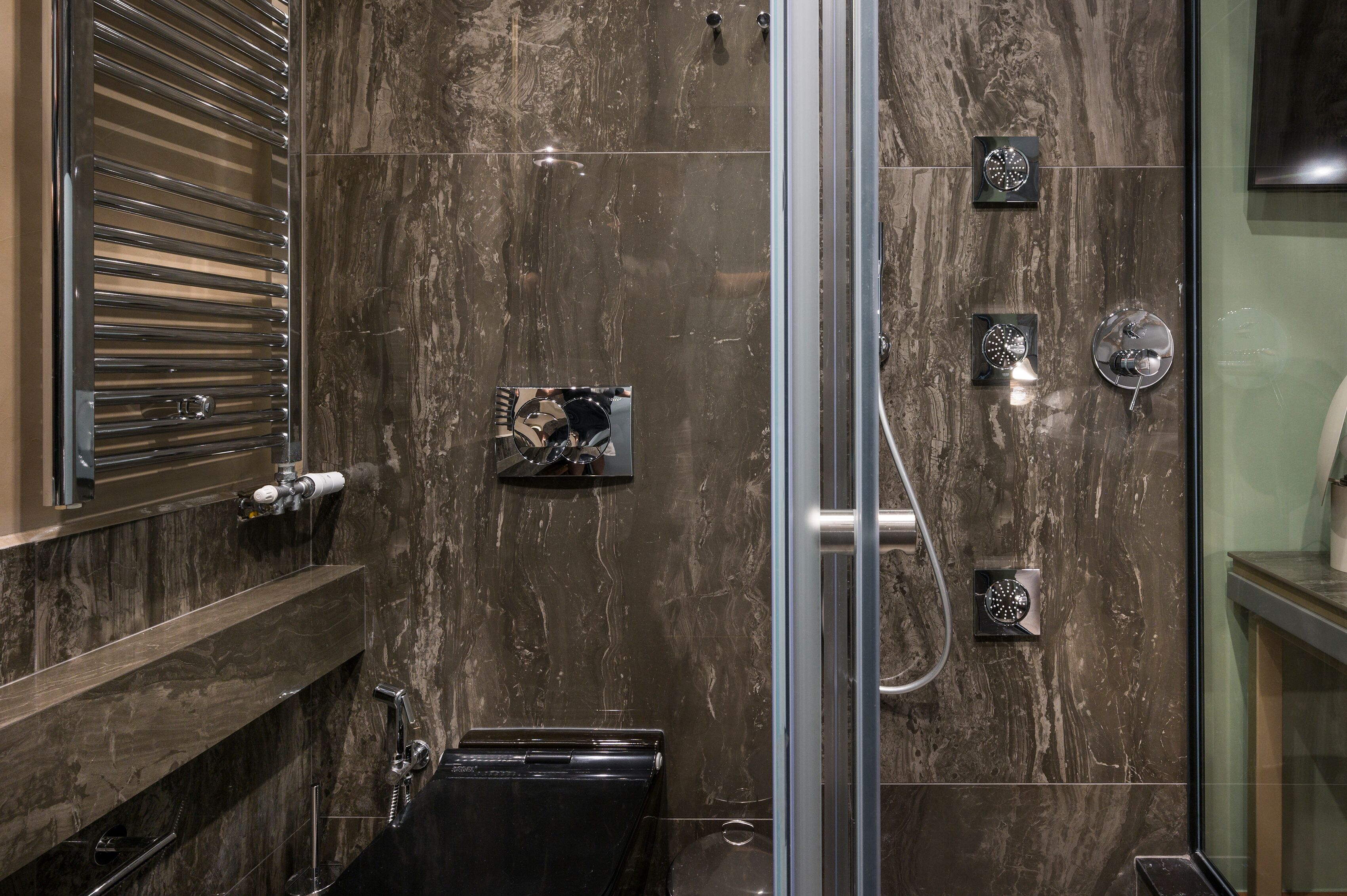 A modern bathroom with a glass shower enclosure, a built-in towel rack, and a marble backsplash.