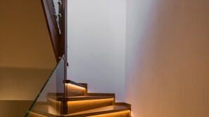 A staircase with wooden steps and glass railings, illuminated by under-cabinet lighting. - Veneri Boutique Suites (Chania)