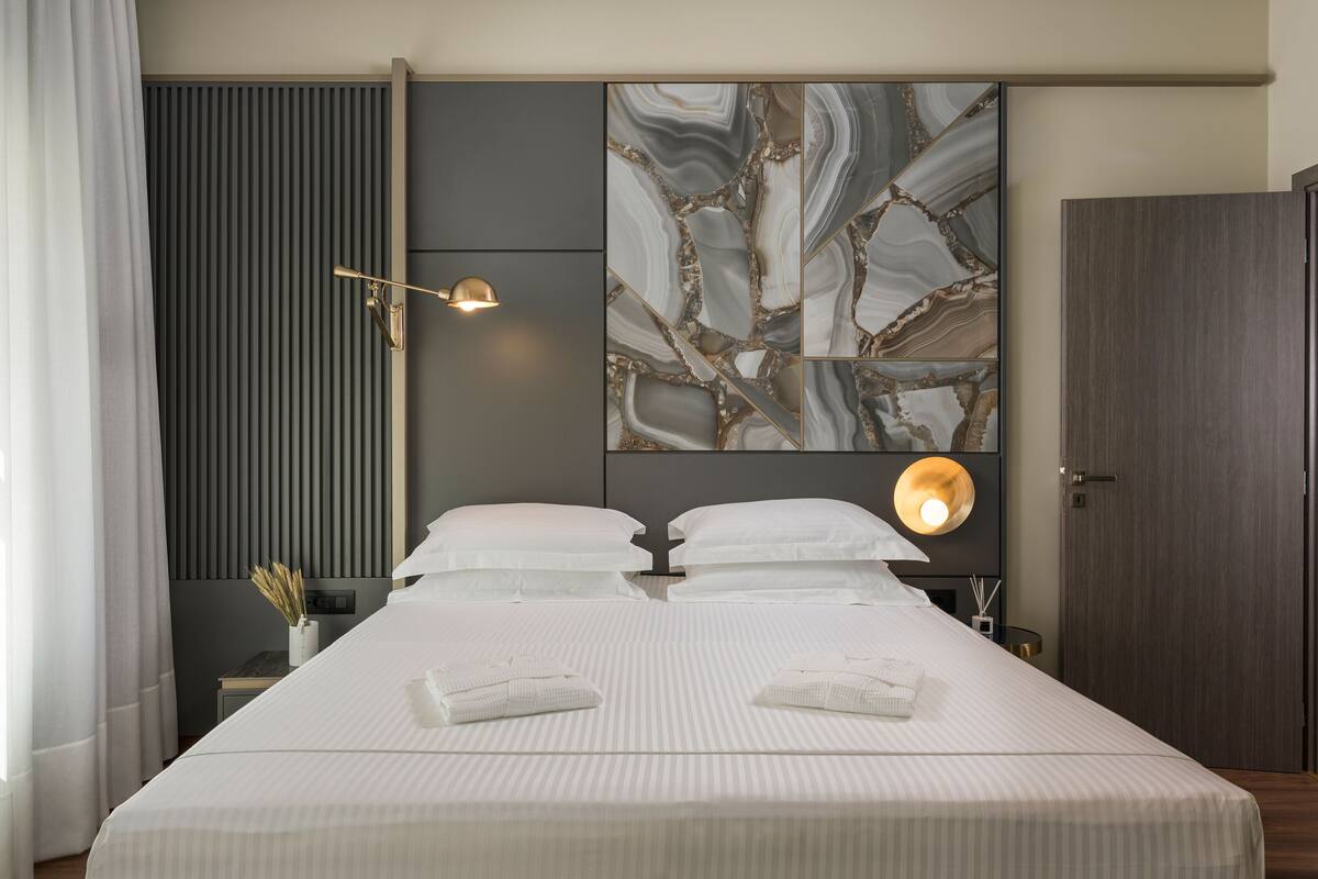 Una habitación de hotel moderna con una cama grande, una obra de arte abstracta en la pared, una lámpara de noche y una puerta de madera.