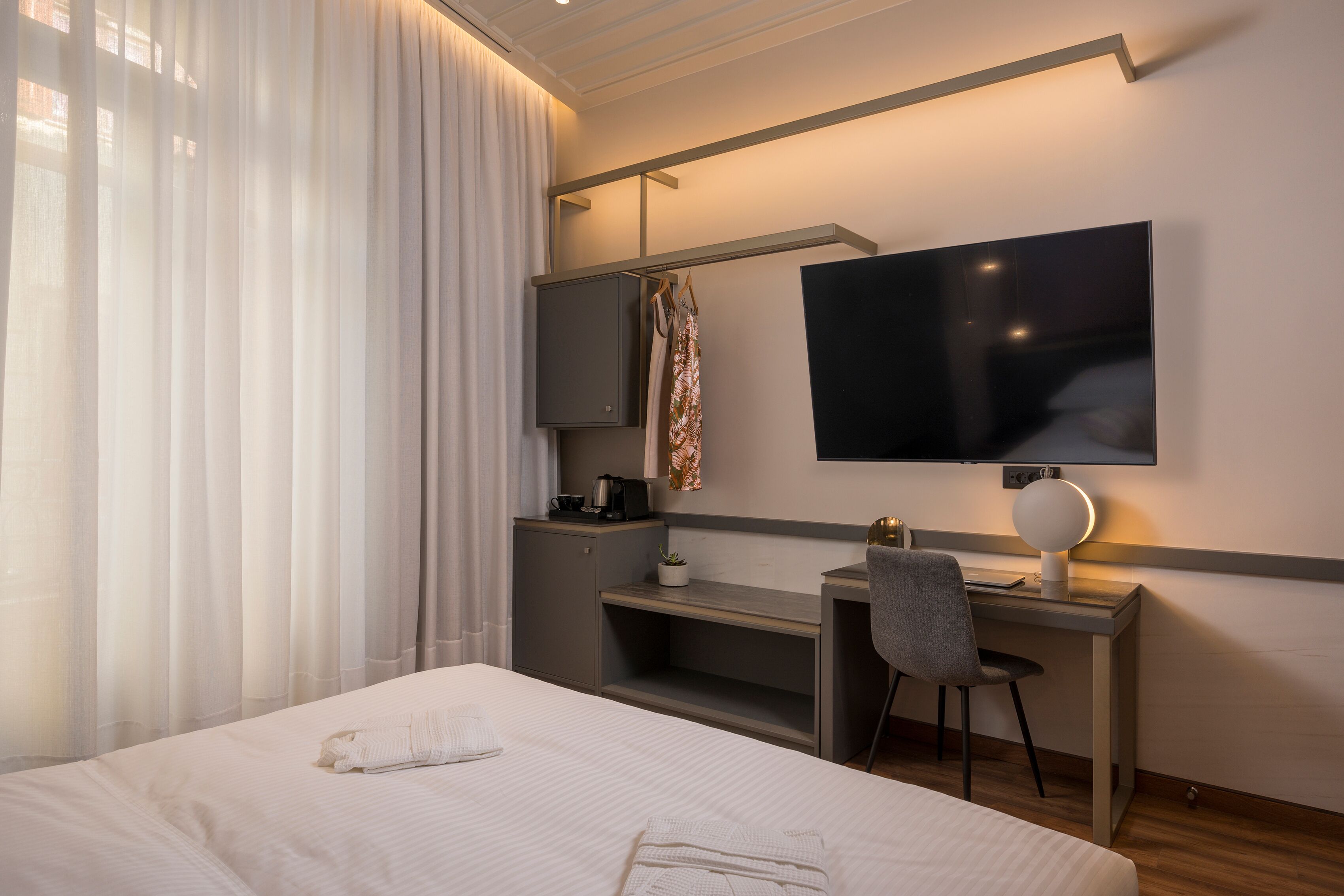 Una habitación de hotel moderna con una cama, un escritorio, una silla, un televisor y un armario.