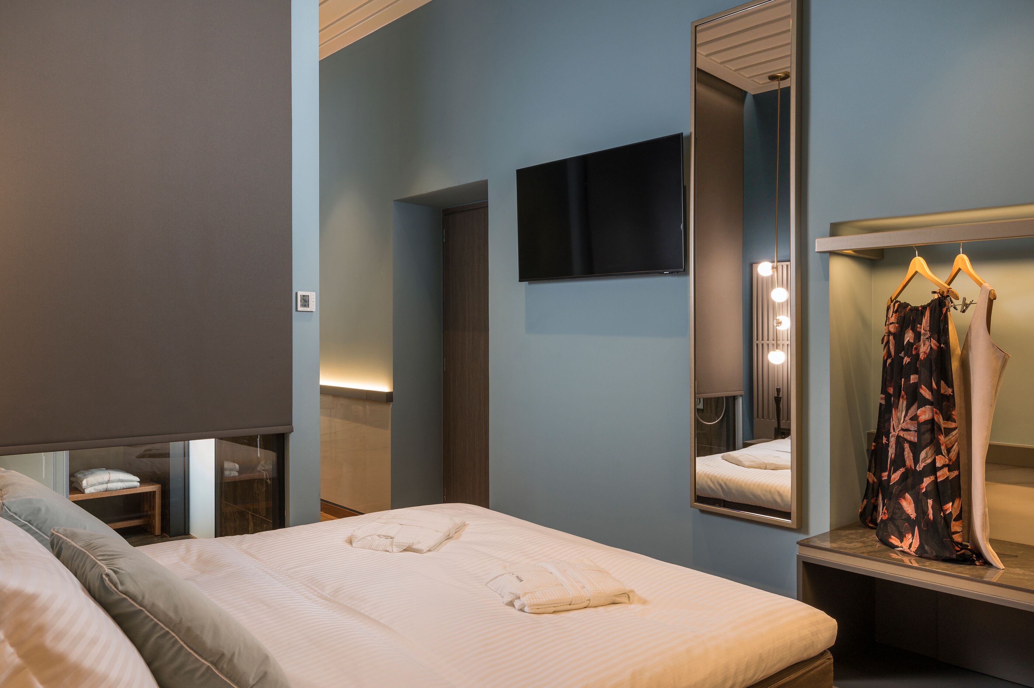 A hotel room with a bed, a TV mounted on the wall, a mirror, and a clothing rack.