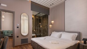 A modern hotel room with a large bed, a sitting area with a sofa, and a bathroom with a glass shower. - Veneri Boutique Suites (Chania)