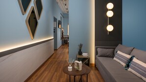 A modern hotel lobby with a wooden floor, a sofa with patterned cushions, and a round table with a decorative vase. - Veneri Boutique Suites (Chania)