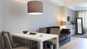 Een moderne woonkamer met een witte eettafel, een grijze bank en een groot raam met gordijnen.