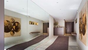 Een moderne gang met een glazen wand, kunstwerken aan de muur en een marmeren vloer.