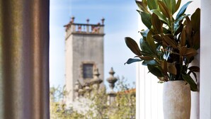 Ein Balkon mit Tisch für Zwei, einem Blumentopf und Blick auf einen Turm.