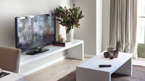 Un salon moderne avec un téléviseur à écran plat, une console blanche, une plante en pot, des bougies et une télécommande posée sur une table basse blanche.