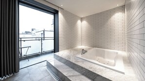 Un baño moderno con una bañera grande, paredes de azulejos blancos y vistas a través de un ventanal.
