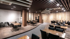 Una sala de conferencias moderna con mesas y sillas de madera, un pasillo alfombrado curvo y un techo alto con vigas a la vista.