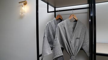 Un baño moderno con un perchero que sostiene dos batas grises, una lámpara de pared y un espejo con marco negro.