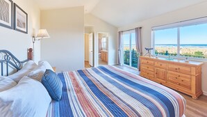 A bedroom with a bed, a dresser, a window with a view of the beach, and a door leading to another room. - OCEAN FRONT, Pets OK, Ping Pong, Near Town and Discovery Trail (Ocean View B) (Long Beach)