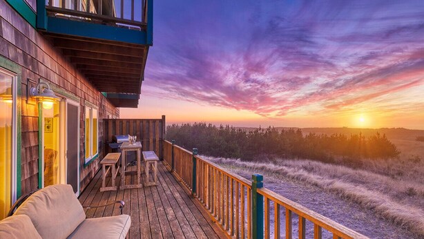 A wooden deck with outdoor seating, overlooking a natural landscape at sunset. - OCEAN FRONT, Pets OK, Ping Pong, Near Town and Discovery Trail (Ocean View A) (Long Beach)