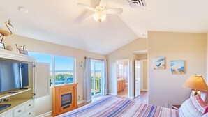 Un dormitorio con una cama grande, televisión, chimenea, ventilador de techo y vistas al exterior.