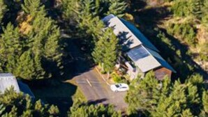An aerial view of a coastal property with a house surrounded by dense forest, a beach in the background, and a clear sky. - OCEAN FRONT, Pets OK, Ping Pong, Near Town and Discovery Trail (Ocean View A) (Long Beach)