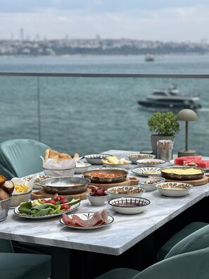 A table set with various dishes and a view of the sea and boats in the background.