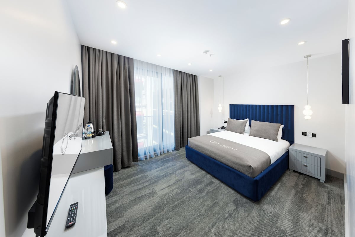 A modern hotel room with a large bed, a desk with a TV, and a window with curtains.