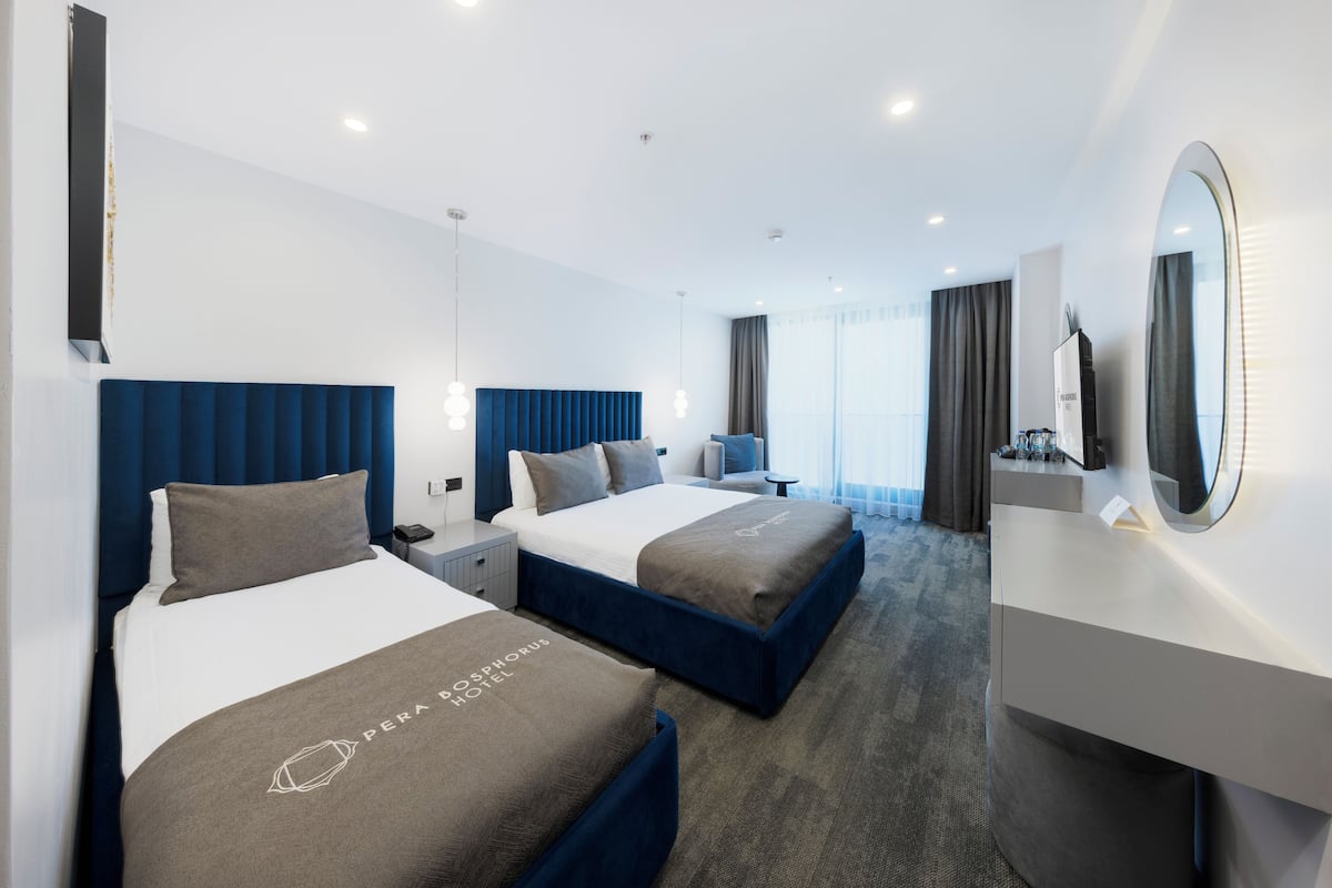 A modern hotel room with two beds, a large mirror, a desk, and a view of the city.
