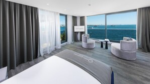 A modern hotel room with a large bed, two armchairs, a small table, and a view of the sea. - Pera Bosphorus Hotel (Istanbul)