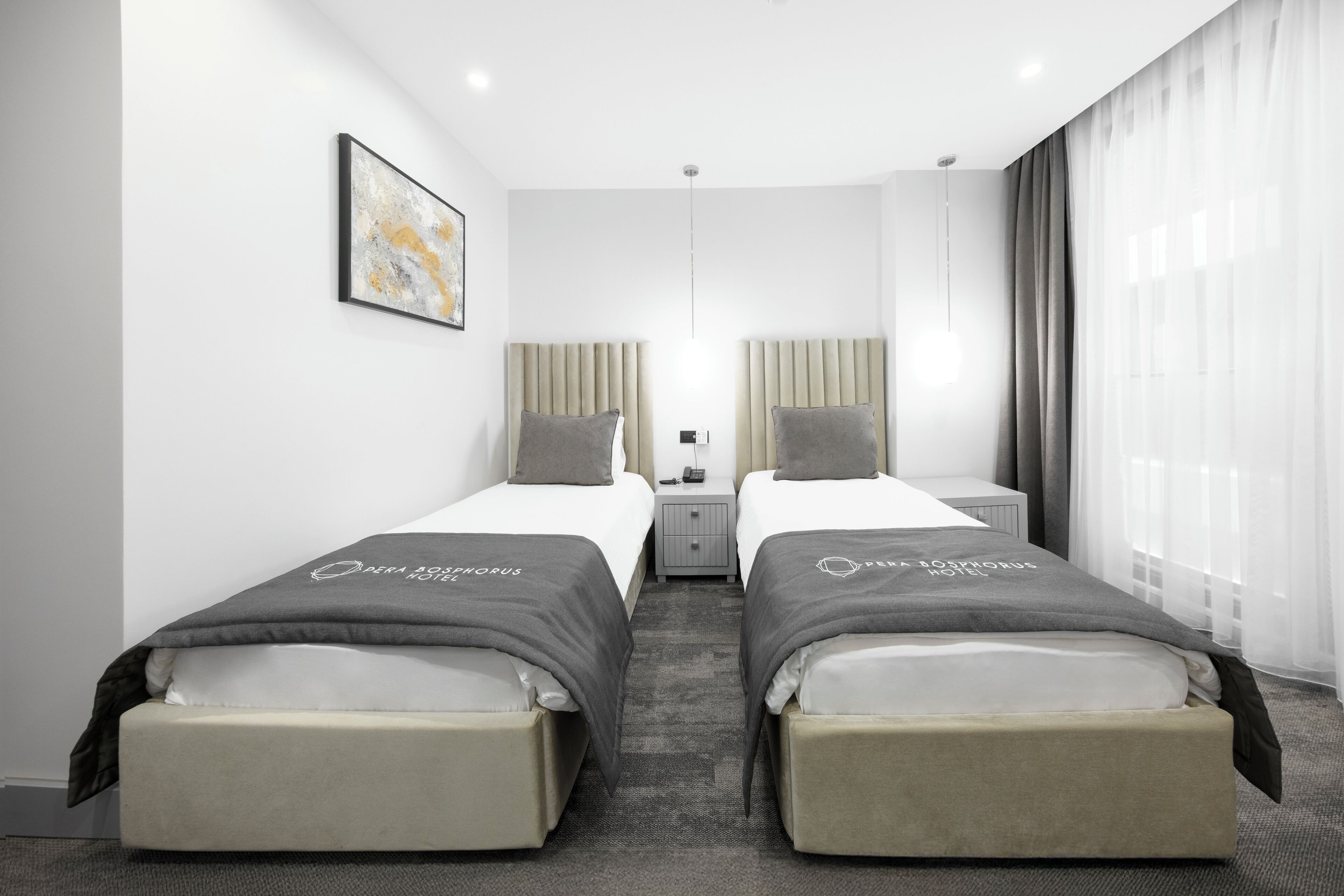 A hotel room with two beds, a nightstand, a lamp, and a window with curtains.