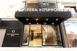 The entrance of the Pera Bosphorus Hotel with a modern facade, glass doors, and a visible staircase leading to the interior.