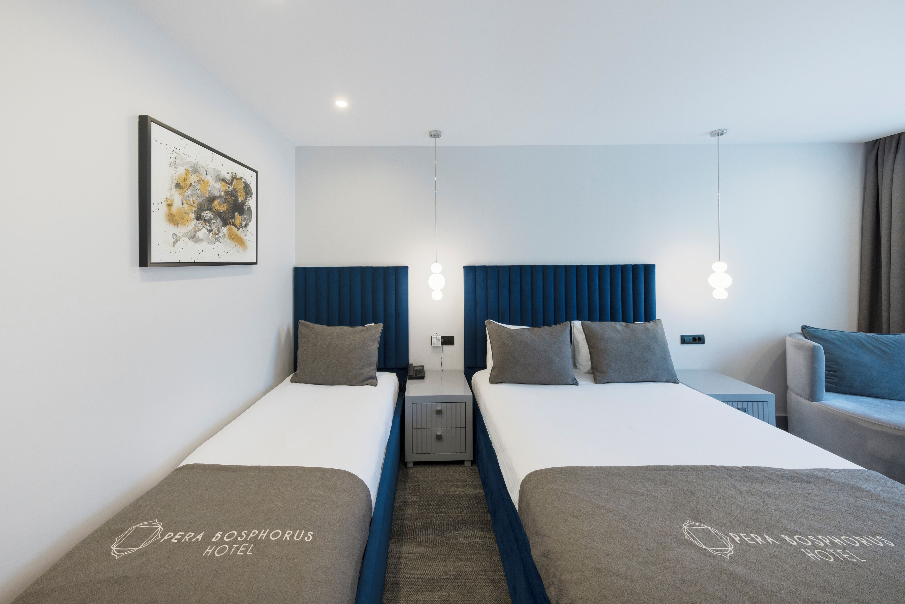 A hotel room with two beds, a nightstand, a lamp, and a painting on the wall.