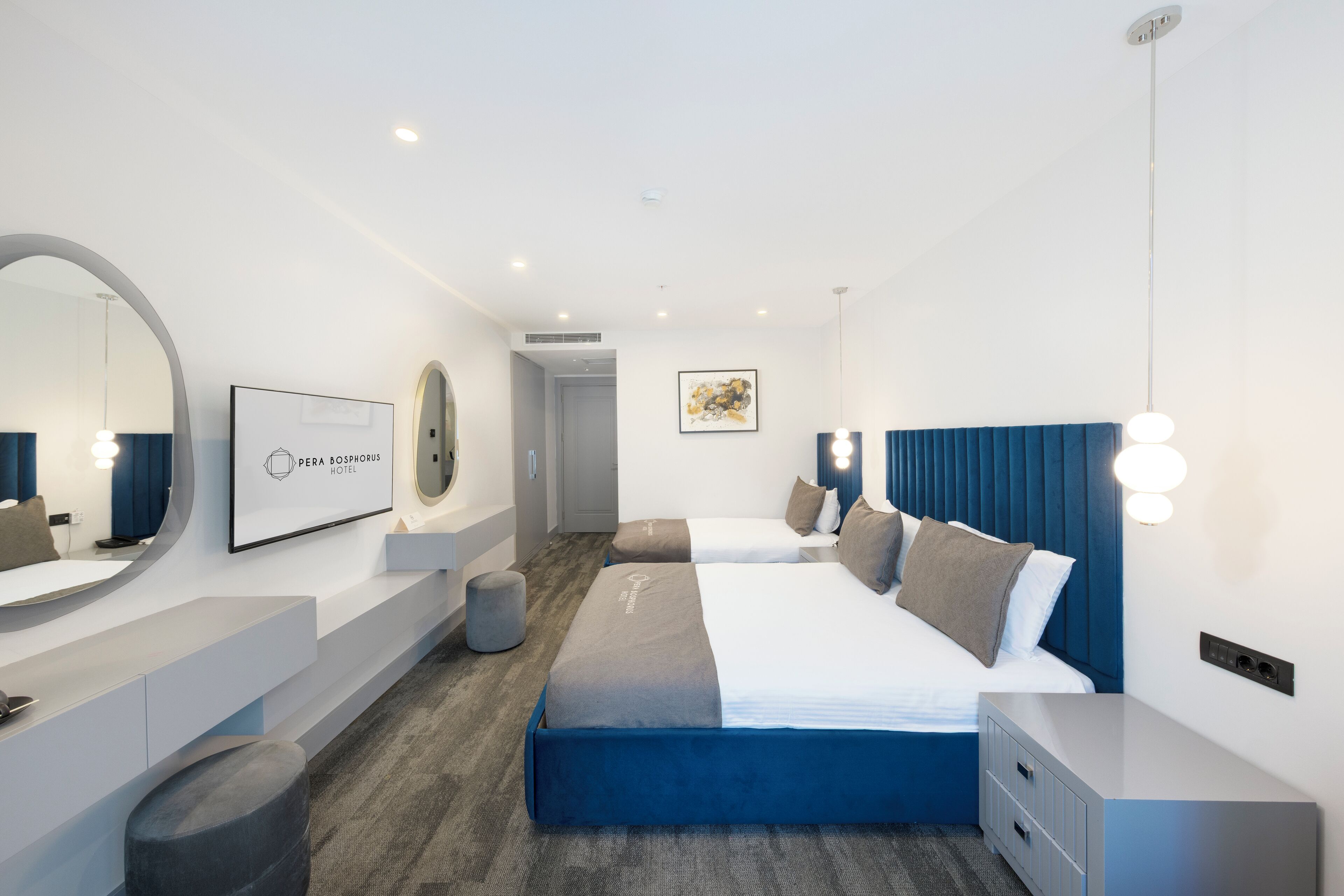 Quarto de hotel moderno com uma cama grande, um espelho redondo, uma escrivaninha e uma obra de arte na parede.