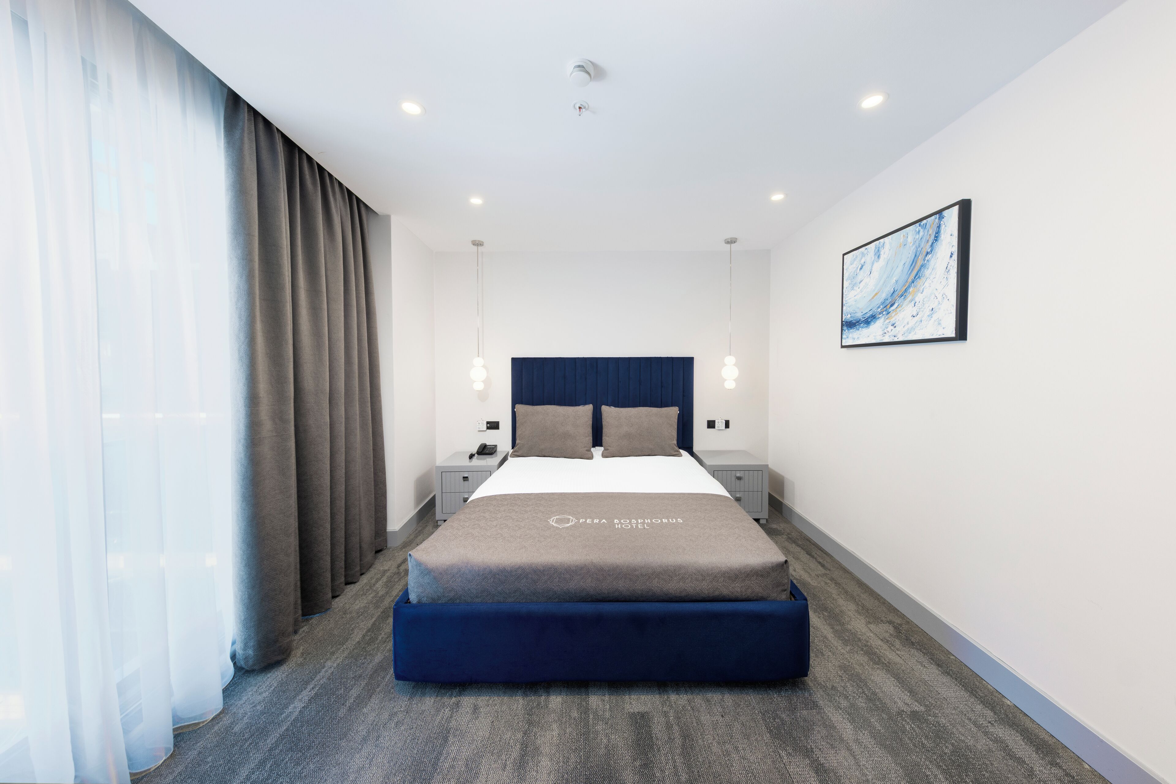 Una habitación de hotel moderna con una cama grande, cabecero, mesitas de noche y un cuadro en la pared.