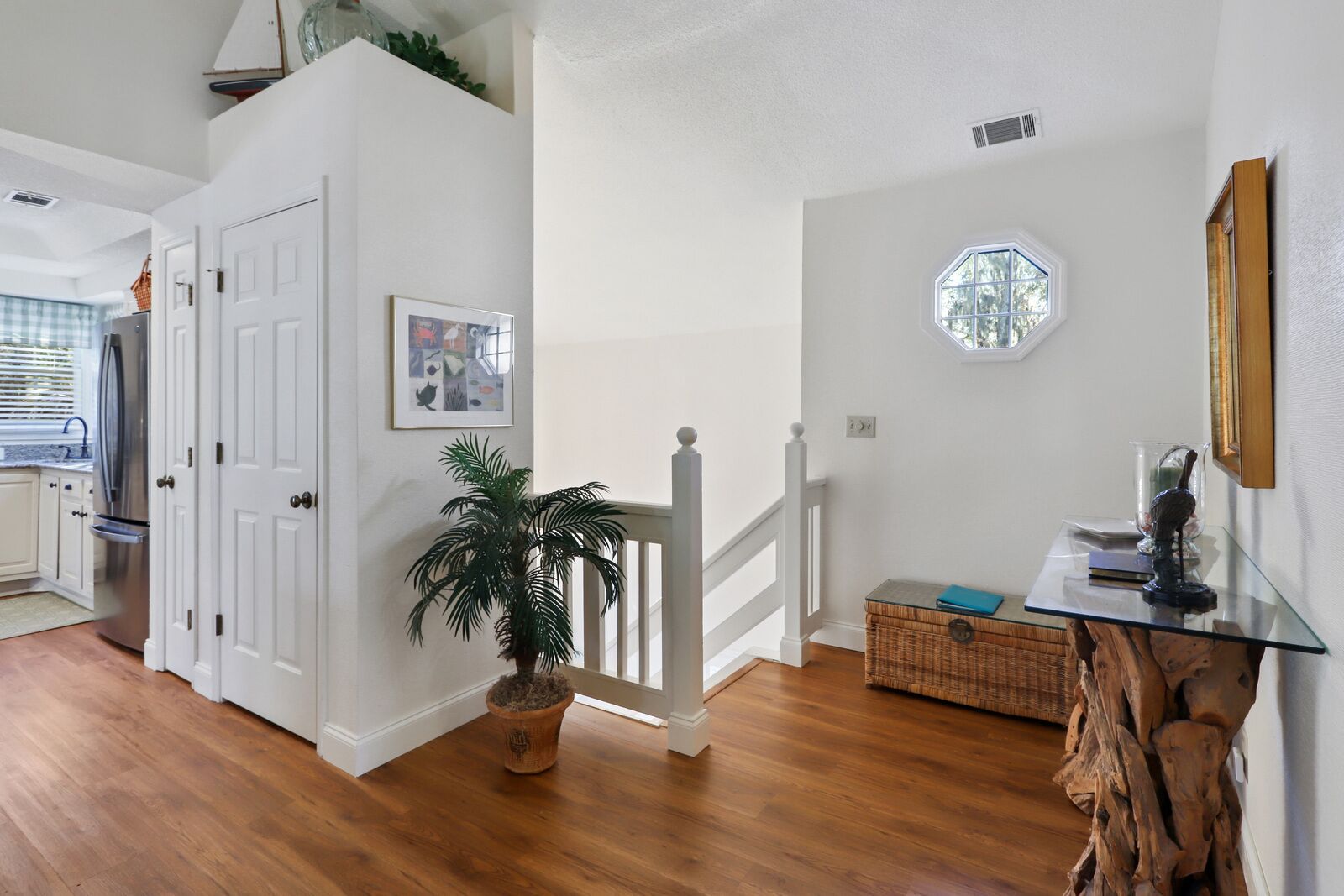 A hallway with wooden flooring, a potted plant, a wicker basket, and a glass table with a blue book and a decorative item.