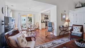 A spacious living room with a sofa, chairs, a dining table, and a kitchen in the background.