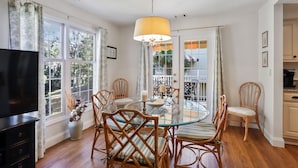 A dining area with a glass table surrounded by wicker chairs, a television, and a chandelier.