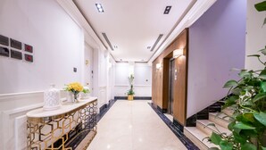 A hotel corridor with a marble floor, a reception desk with a vase of flowers, and a staircase with a plant on the right. - Mabaat - Al Yasmeen - 353 (Riyadh)