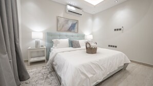 A modern bedroom with a large bed, bedside lamps, a wall-mounted air conditioner, and a ceiling light. - Mabaat - Al Yasmeen - 353 (Riyadh)