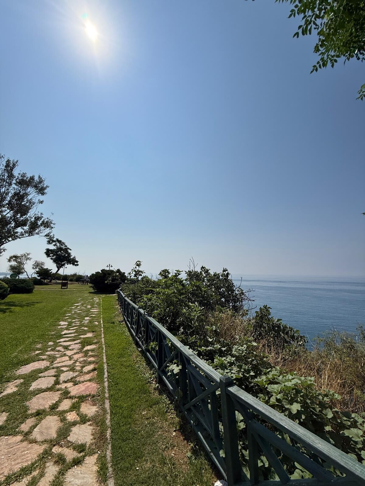 A pathway with stone slabs and a metal railing, leading to a scenic overlook with a view of the sea.