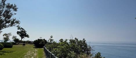A pathway with stone slabs and a metal railing, leading to a scenic overlook with a view of the sea.