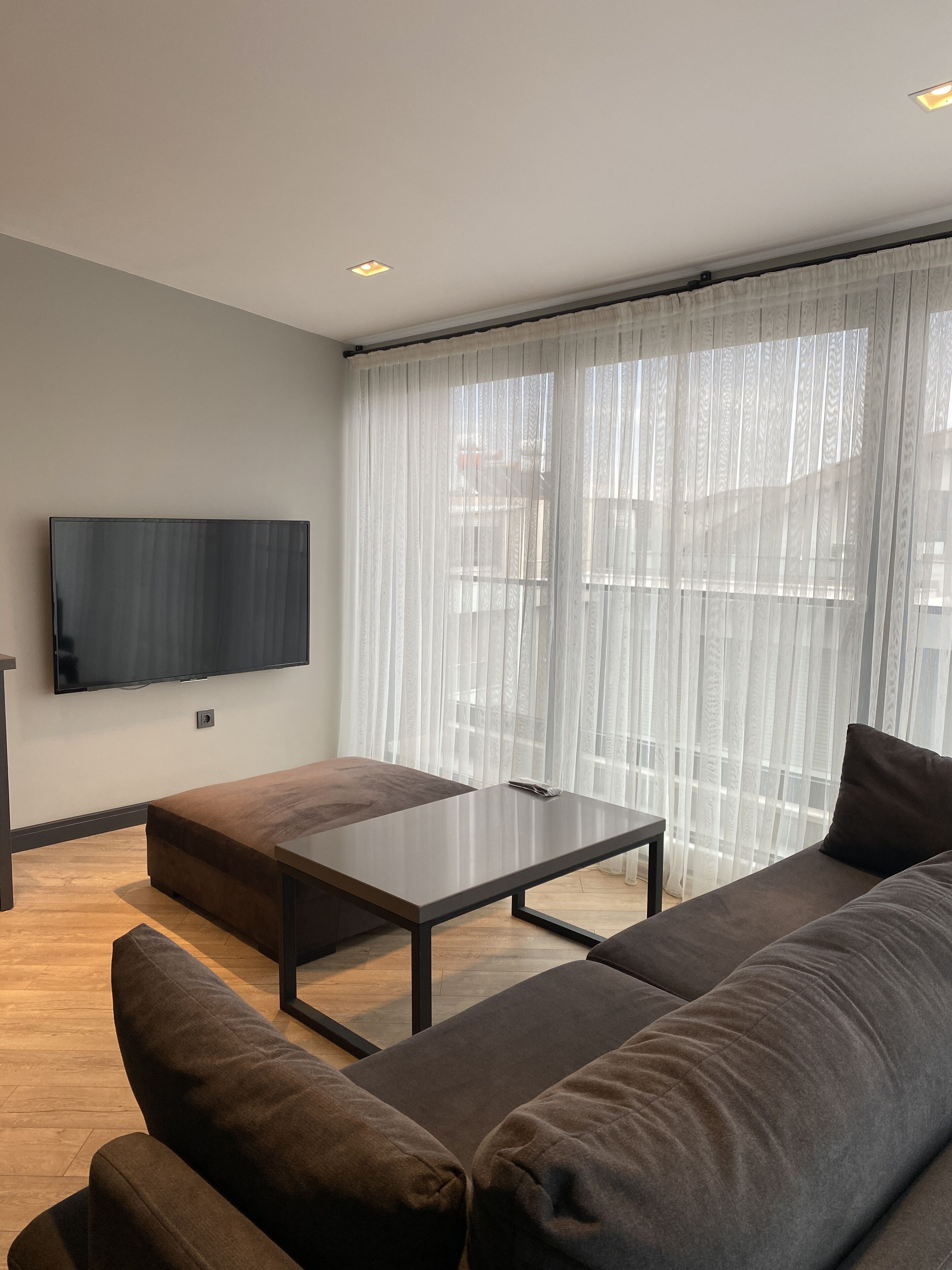Una sala de estar moderna con un televisor de pantalla plana grande montado en la pared, una mesa de centro de madera oscura y un sofá seccional marrón grande.