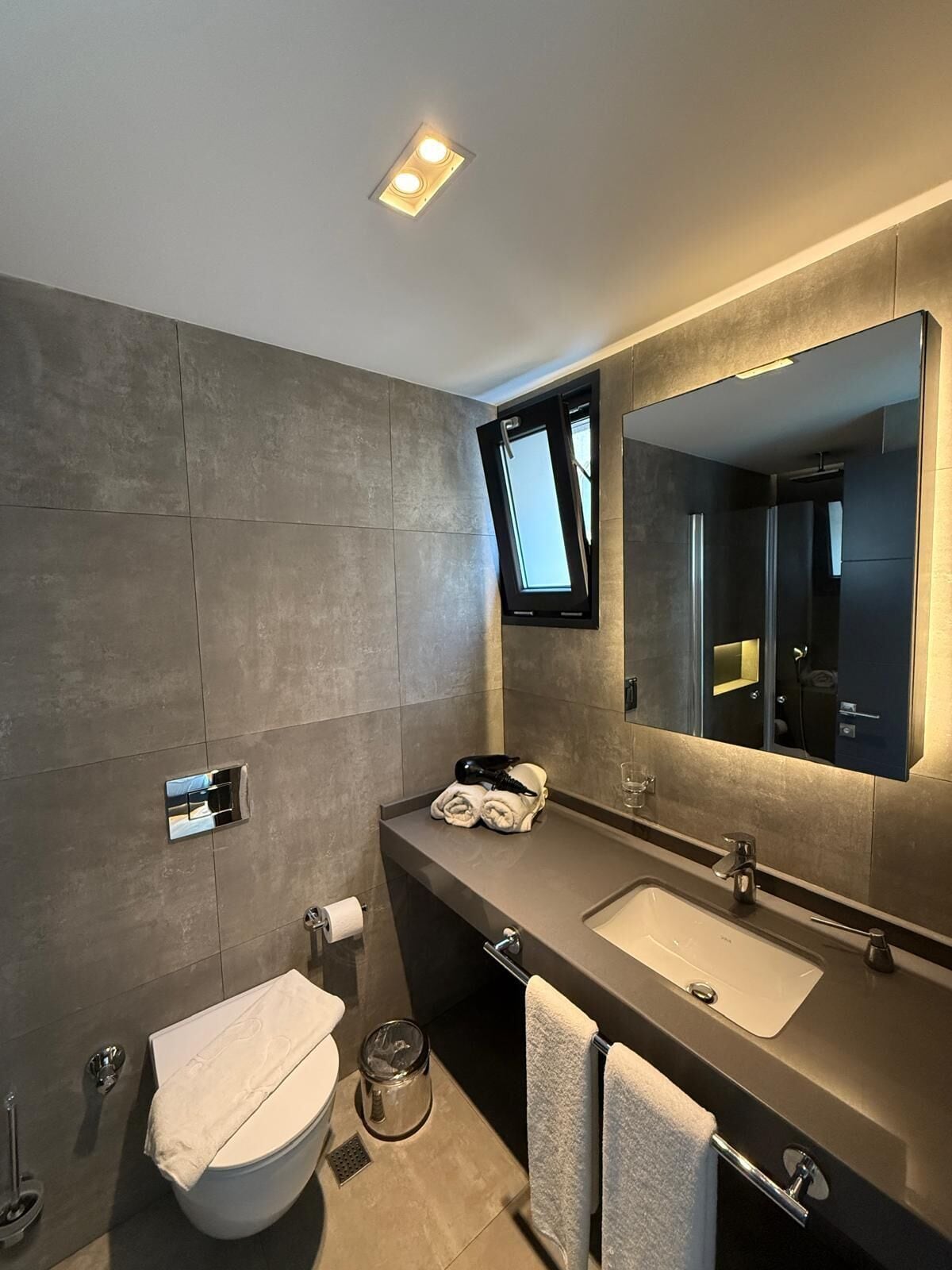 Un baño moderno con un espejo grande, inodoro, lavamanos y ducha.
