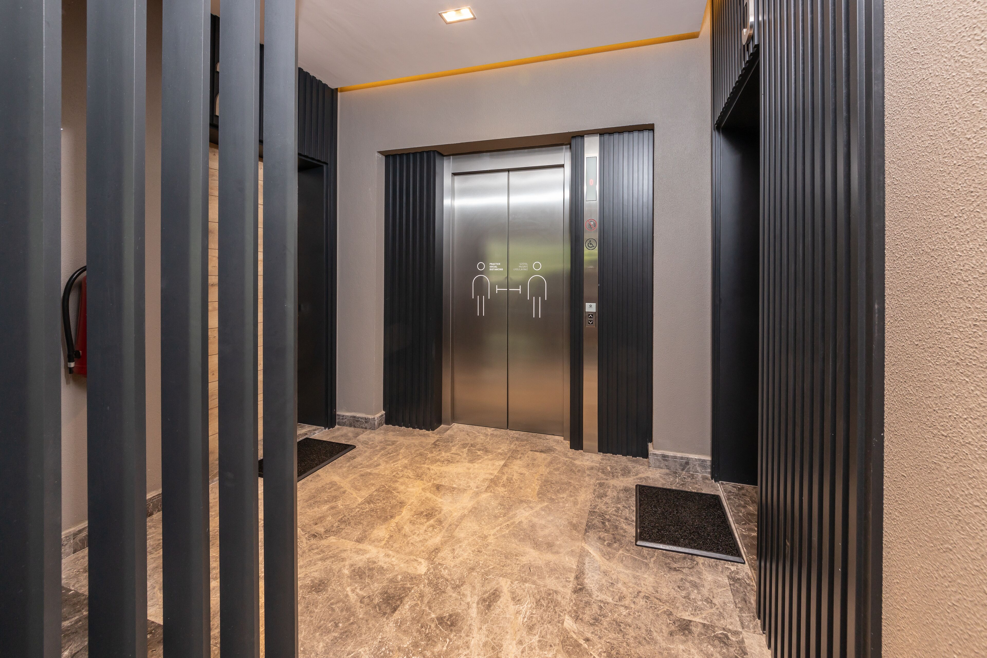 A modern elevator with a metallic finish, flanked by dark vertical panels and a marble-tiled floor.